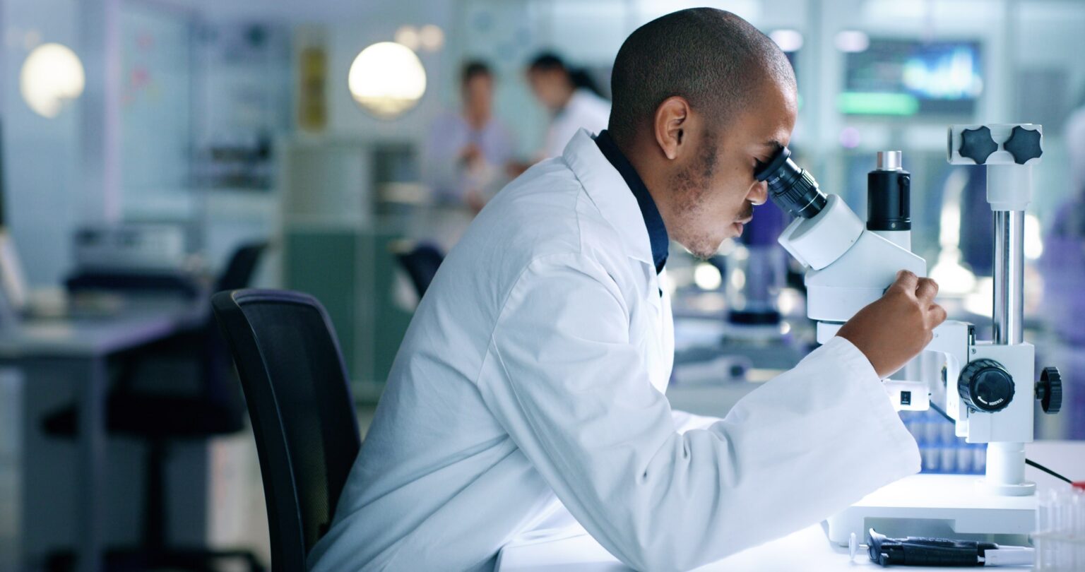Scientist looking through a microscope in the laboratory and using the STARLIMS laboratory information management system