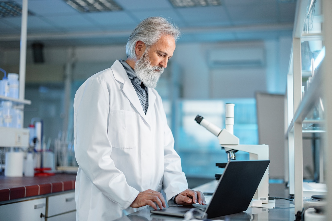 Man works at a laptop in a laboratory in front of a microscope.