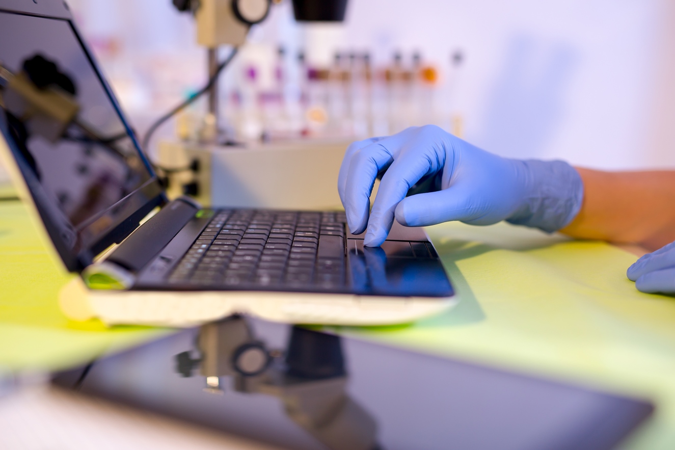 A person with sterile gloves works on a laptop.