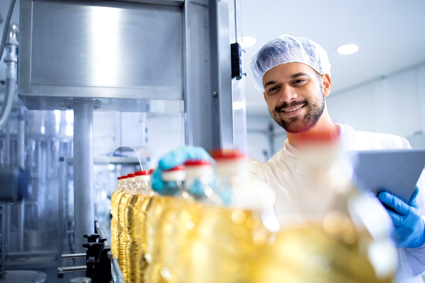 Industrial production of oil and factory worker performing quality control on automated machine.