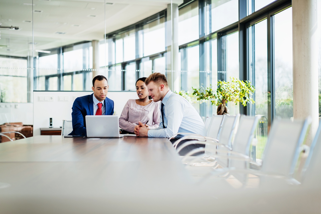 A meeting between three business professionals sitting at a conference table in a modern office.