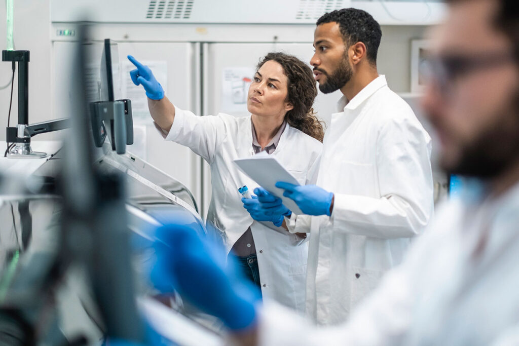 Two scientists in lab coats reviewing data on a screen in a laboratory.